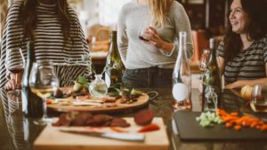 Three women drinking wine while preparing a meal